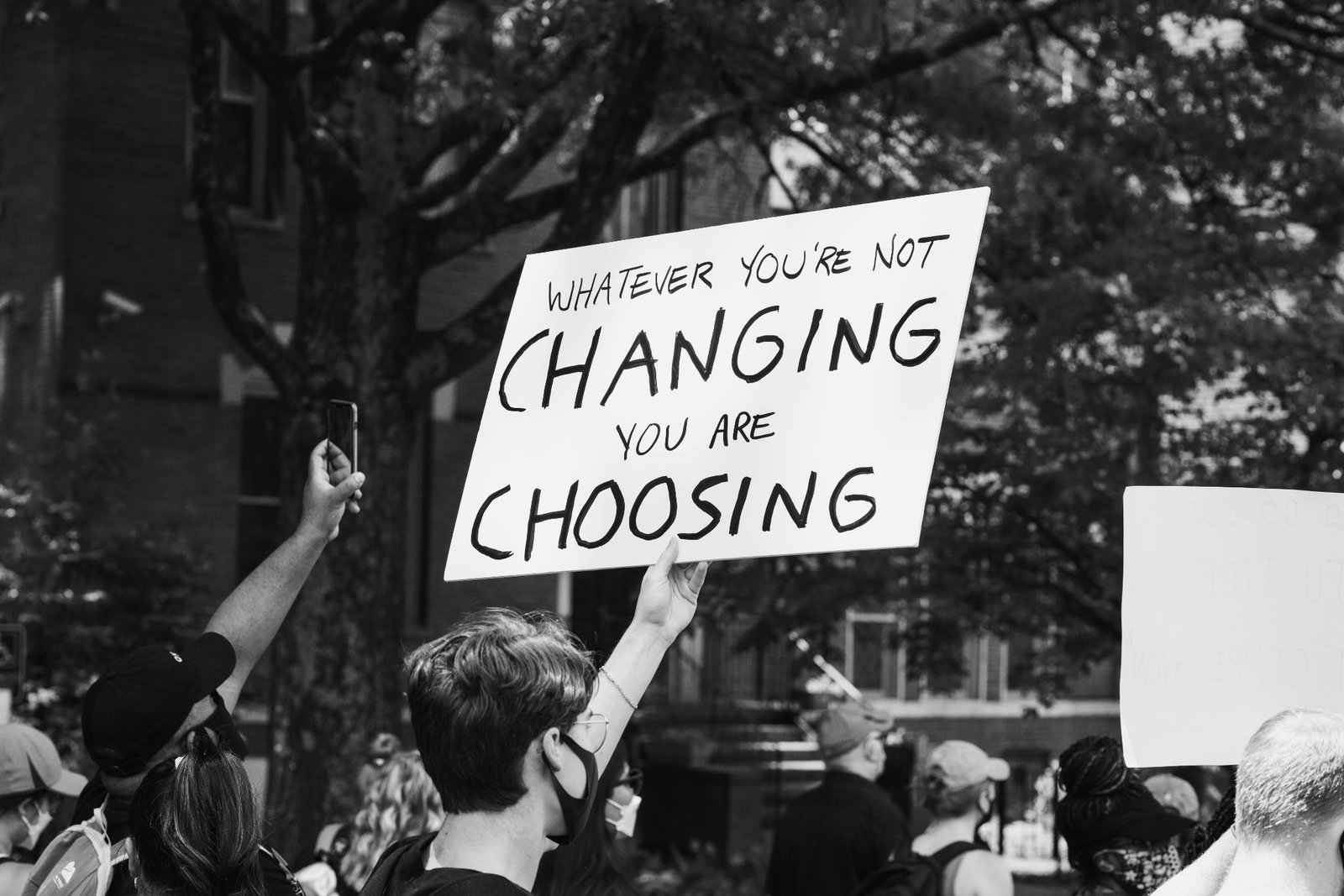 Community members participating in a protest holding a sign that reads Whatever you are not changing you are choosing